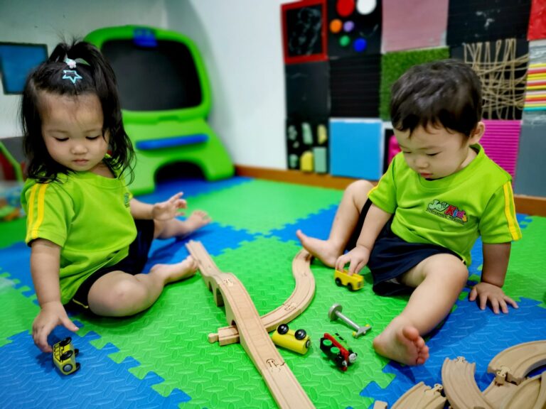 Toddlers building a wooden train track together in the playroom at JoyKids International Preschool